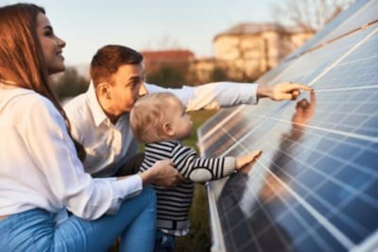 un couple avec un enfant se tient accroupi devant des panneaux photovoltaïques image illustrant alerte attention aux faux rachats de credit