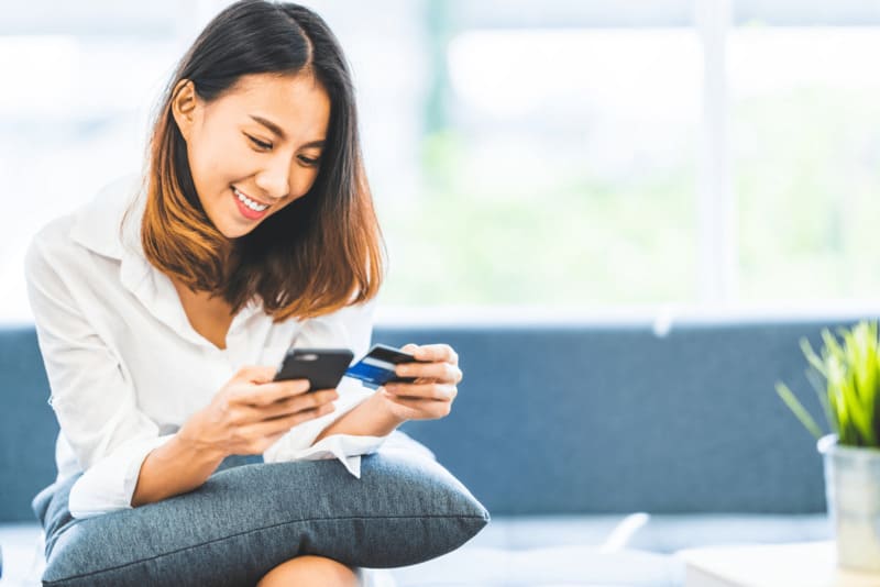 Jeune femme souriante regardant sur son téléphone ses opérations de carte bancaire