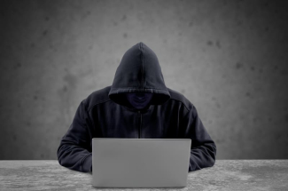 escroc en capuche cachant son visage devant son ordinateur