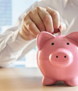 Main déposant une pièce dans une tirelire rose en forme de cochon