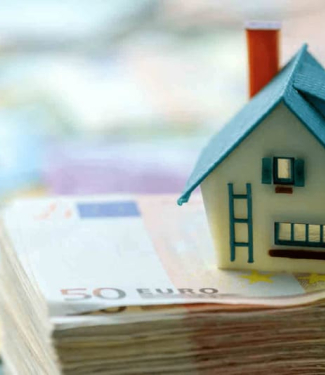 Maison miniature posée sur un tas de billets pour illustrer article sur les arnaques à la location saisonnière