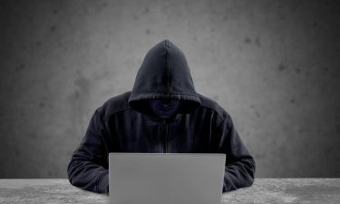 escroc en capuche cachant son visage devant son ordinateur