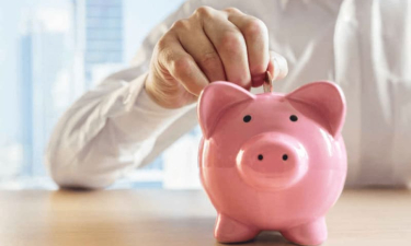 Main déposant une pièce dans une tirelire rose en forme de cochon